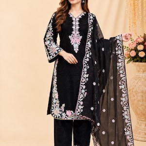 Könnte beinhalten: Ein schwarzes dreiteiliges Outfit bestehend aus einer langärmeligen Tunika, einer Hose mit geradem Bein und einem passenden Dupatta. Die Tunika und der Dupatta sind an den Rändern mit aufwendigen Blumenstickereien in Rosa, Weiß und Hellblau verziert.