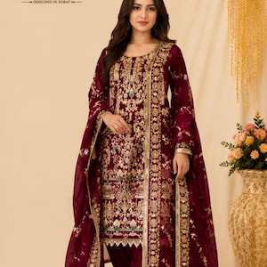 Può includere: Un completo salwar kameez color bordeaux profondo con intricati ricami dorati e dettagli in paillettes. La tunica a maniche lunghe presenta uno scollo rotondo, abbinata a pantaloni coordinati e a un dupatta trasparente ricamato.