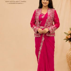 Op de afbeelding: Een levendige fuchsia sari gecombineerd met een bijpassende mouwloze blouse en een jasje met lange mouwen. Het jasje heeft ingewikkeld zilverkleurig borduurwerk op de voorpanden en manchetten. De sari is voorzien van een decoratieve zilveren rand.