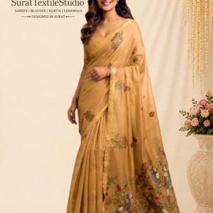 Könnte beinhalten: Ein goldbrauner Sari mit einer V-Ausschnitt-Bluse und einem transparenten Stoffdrapé, das mit gestickten Blumenmustern und bunten Vogelmotiven verziert ist. Das Kleidungsstück hat einen Goldrand und trägt den Text SuratTextileStudio.