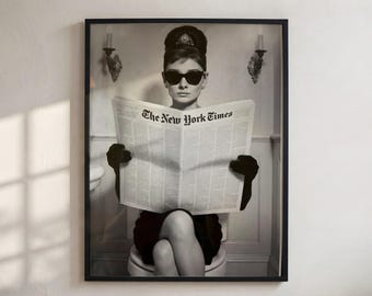 May include: A black and white framed print featuring a person with an updo hairstyle, wearing dark sunglasses and black gloves, sitting on a toilet while holding a newspaper with the text The New York Times clearly visible on the front page.