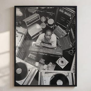 Puede incluir: Una fotografía enmarcada en blanco y negro que muestra a una persona en el centro de un estudio de música rodeada de varios equipos de audio, incluyendo un sintetizador Roland JP-8000, varias consolas de mezcla y dos tocadiscos.