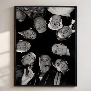 May include: A black and white framed print featuring a low-angle, circular composition of several individuals looking downward. The group includes a person wearing glasses and a hat, and another person holding a cigar, all captured in a high-contrast, monochromatic photographic style.