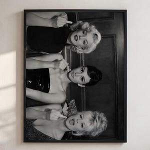 May include: A black and white framed wall art print featuring three iconic figures. The top figure has blonde hair, the middle figure has dark hair, and the bottom figure has blonde hair. All three are making a middle finger gesture in this portrait.