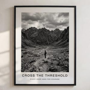 Pode incluir: Uma impressão artística emoldurada a preto e branco com uma paisagem montanhosa e uma pessoa de pé num caminho. O texto na parte inferior diz CROSS THE THRESHOLD e EVERY DOOR ASKS FOR COURAGE numa fonte sem serifa sobre uma margem branca.