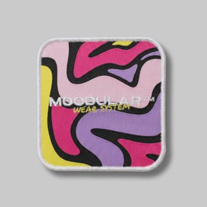Op de afbeelding: Een vierkante geborduurde patch met afgeronde hoeken en een levendig, abstract golvend patroon in tinten roze, paars, geel en zwart. De tekst MOODULAR WEAR SYSTEM is in het wit en geel in het midden geborduurd.