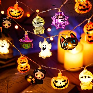 Könnte beinhalten: Eine Halloween-LED-Lichterkette mit verschiedenen beleuchteten Figuren, darunter orangefarbene Kürbisse, weiße Geister, eine Mumie, ein schwarzes Katzengesicht, eine Hexe und ein violettes Spinnennetz. Die dekorativen Lichter strahlen warmes Licht aus.