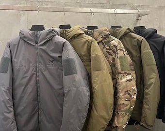 Könnte beinhalten: Eine Reihe von fünf Kapuzenjacken, die an einer Stange hängen. Die Jacken sind in Grau, Olivgrün, Camouflage, Dunkeloliv und Schwarz gehalten. Jede Jacke verfügt über einen durchgehenden Frontreißverschluss, eine Kapuze und ein Klettband.