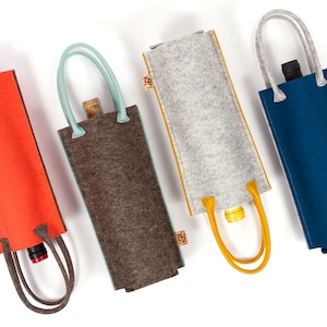 Könnte beinhalten: Vier Filz-Weinflaschentaschen mit verschiedenen Farbkanten. Die Taschen sind grau mit gelber Kante, braun mit hellblauer Kante, orange mit brauner Kante und blau mit gelber Kante.