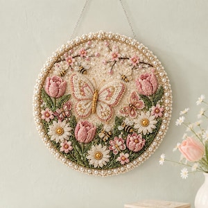Könnte beinhalten: Ein kreisförmiger Wandbehang mit aufwendigen Perlenstickereien eines großen zentralen Schmetterlings, kleineren Schmetterlingen, Bienen, rosa Tulpen, weißen Gänseblümchen und Kirschblüten, eingefasst von einem Rand aus kleinen weißen Perlen.