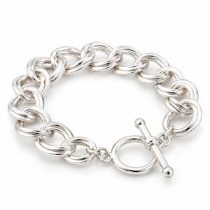 May include: A polished silver-tone chain link bracelet featuring a series of interconnected double circular links. The bracelet is secured with a toggle clasp consisting of a circular ring and a matching T-bar component, creating a classic design.