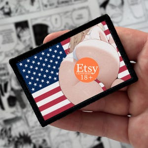 Könnte beinhalten: Ein rechteckiger Aufnäher mit schwarzem gesticktem Rand, der eine Grafik der Flagge der Vereinigten Staaten und eine Anime-Illustration einer Figur zeigt. Die Mitte ist durch einen runden orangefarbenen Aufkleber mit dem Text Etsy CENSORED 18+ verdeckt.
