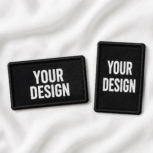 Op de afbeelding: Twee rechthoekige zwarte patches met geborduurde randen. De ene patch is horizontaal georiënteerd en de andere verticaal. Beide zijn voorzien van de witte tekst YOUR DESIGN, gecentreerd in een vetgedrukt schreefloos lettertype.