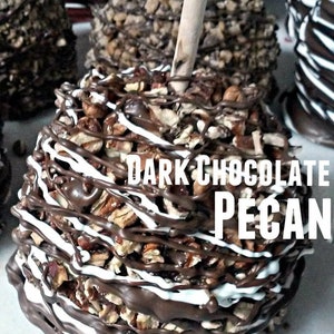 May include: Dark chocolate covered apple with white chocolate drizzle and chopped pecans. The apple is on a white surface and the text "DARK CHOCOLATE PECAN" is on the apple.
