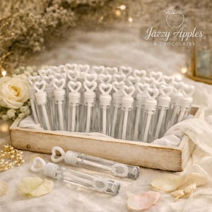 May include: A wooden tray filled with bubble wands. The wands have clear tubes and white heart-shaped handles. Two bubble wands are in front of the tray. The image has a soft, romantic aesthetic with flowers and the text "Jazzy Apples & Chocolates".