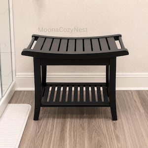 May include: A black wooden shower bench with a curved slatted seat and a lower slatted storage shelf. The bench features four sturdy legs and the text MoonaCozyNest is visible above the seat. The design includes horizontal slats.