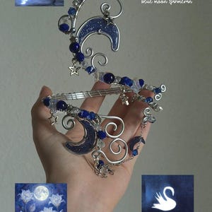 May include: A silver-toned wire hand chain featuring dark blue crescent moon charms, small star charms, and deep blue beads. The jewelry piece includes intricate wire-wrapped swirls and delicate chain links, accented with clear and blue glass beads.