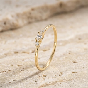 May include: A thin gold ring featuring a central marquise-cut clear stone flanked by two smaller round-cut clear stones. The band is polished yellow gold, and the setting holds the three stones in a horizontal arrangement along the top of the ring.