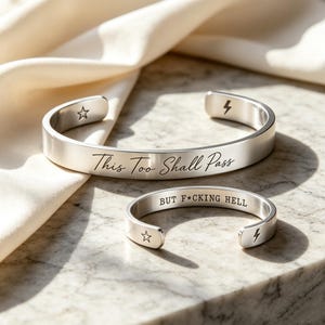Può includere: Due bracciali a fascia in metallo color argento. Il bracciale più grande è inciso con il testo "This Too Shall Pass" e presenta un simbolo a forma di stella e fulmine. Il bracciale più piccolo reca l'incisione "BUT F*CKING HELL" e una stella e un fulmine.