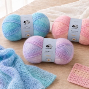 May include: Three skeins of soft, fuzzy yarn in blue, pink, and purple ombre gradients, each wrapped in a MuYuan label with a sheep logo. A knitted blue and purple scarf and a small pink crocheted square are displayed alongside the yarn skeins.