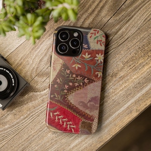 Puede incluir: Una funda para smartphone con un diseño de patchwork que presenta varios patrones florales en tonos rojo, rosa, crema y marrón. El diseño incluye detalles de estilo bordado, bordes cosidos y motivos botánicos en toda la superficie.