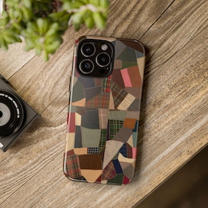 May include: A smartphone case featuring a multi-coloured patchwork design composed of various fabric textures and patterns, including plaid, solid brown, tan, green, and blue segments, with a prominent triple-lens camera cutout at the top.