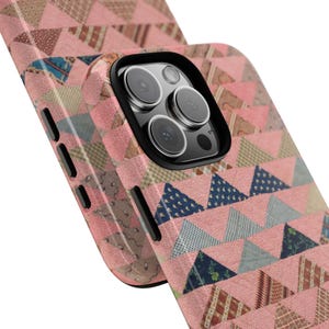 Puede incluir: Una funda protectora para teléfono con un patrón geométrico repetitivo de triángulos en tonos rosa, azul y marrón. La funda tiene un marco negro para la cámara y botones laterales negros, diseñada para un smartphone con triple lente.