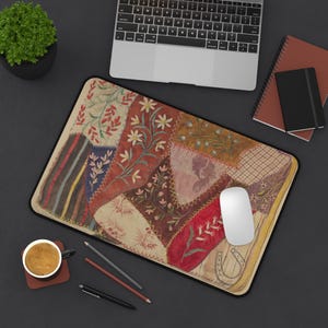 Può includere: Un tappetino da scrivania rettangolare caratterizzato da un design patchwork con vari motivi floreali e botanici nelle tonalità del rosso, marrone, crema e blu. La superficie presenta sezioni cucite con fiori, foglie e motivi geometrici ricamati.