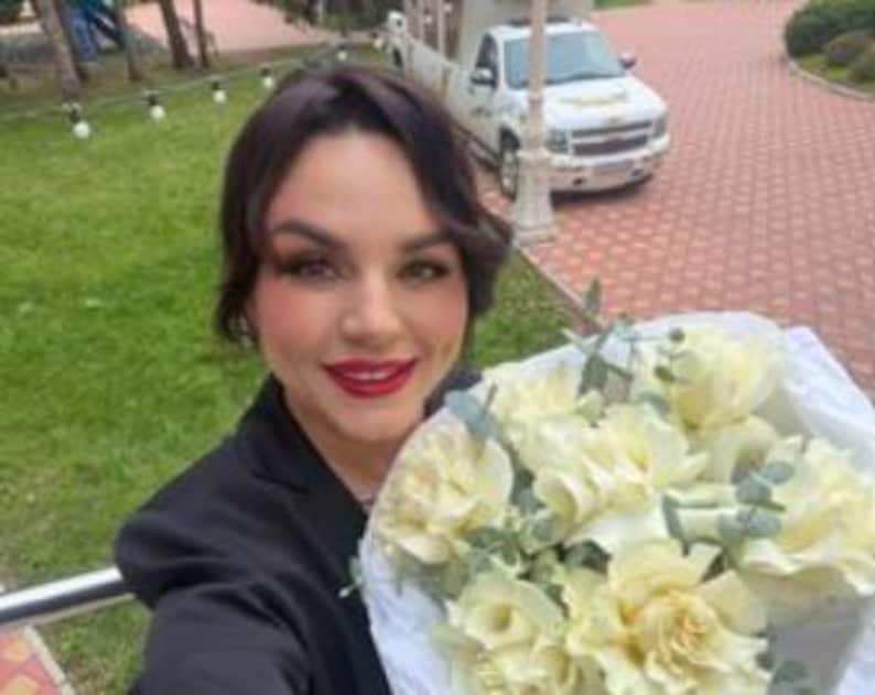 K&ouml;nnte beinhalten: Ein Blumenstrau&szlig; aus wei&szlig;en Rosen mit gr&uuml;nen Eukalyptusbl&auml;ttern, eingewickelt in wei&szlig;es Papier. Die Blumen sind in einem runden B&uuml;ndel angeordnet und zeigen zahlreiche bl&uuml;hende Bl&uuml;tenbl&auml;tter sowie gr&uuml;ne Blattakzente im gesamten Arrangement.