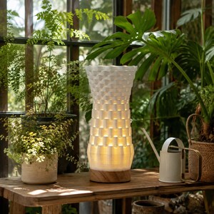 May include: A cylindrical table lamp with a white, 3D-printed, woven-style lattice shade that emits a warm internal glow. The lamp features a circular wooden base and sits upright on a flat surface, showcasing a textured, repeating pattern.