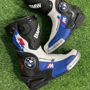 Puede incluir: Un par de botas de moto BMW Motorrad en negro, blanco y azul con el logotipo de BMW, el logotipo M y el texto BMW Motorrad. Las botas tienen un diseño de caña alta con paneles protectores, un logotipo R rojo y deslizadores de punta plateados.