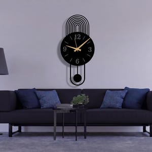 May include: A black wall clock with a circular face, gold-colored hands, and numerals at the 3, 6, 9, and 12 positions. The clock features a decorative arched top design with vertical lines and a pendulum component extending below the main dial.