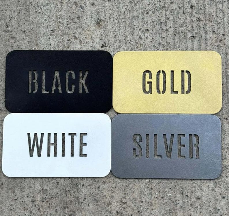 May include: Four rectangular metal plates with rounded corners, each featuring a laser-cut word. The top left plate is black with the word BLACK, the top right is gold with GOLD, the bottom left is white with WHITE, and the bottom right is silver with SILVER.