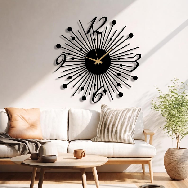 Puede incluir: Un reloj de pared negro con dise&ntilde;o de rayos de sol, centro circular, radios met&aacute;licos finos rematados con peque&ntilde;as esferas y grandes n&uacute;meros estilizados para el 3, 6, 9 y 12. Las manecillas doradas contrastan con el marco de color negro.