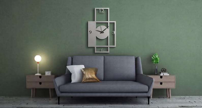 Pu&ograve; includere: Un orologio da parete rettangolare in metallo argentato con una cornice geometrica a sezioni aperte e un quadrante circolare centrale. Il quadrante mostra i numeri 3, 6, 9 e 12 in un semplice carattere sans-serif con due sottili lancette nere.