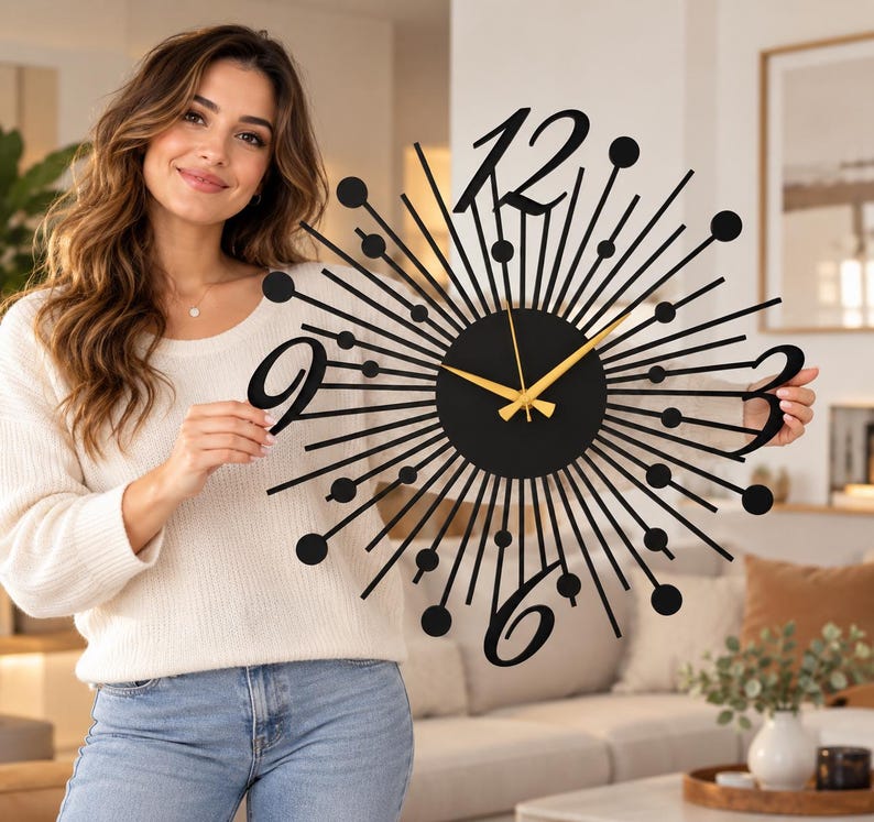 Puede incluir: Un reloj de pared negro con dise&ntilde;o de rayos de sol, centro circular, radios met&aacute;licos finos rematados con peque&ntilde;as esferas y grandes n&uacute;meros estilizados para el 12, 3, 6 y 9. El reloj tiene tres manecillas finas de color dorado.