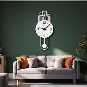 May include: A white wall clock featuring a circular face with black numerals at the 3, 6, 9, and 12 positions, black hour and minute hands, a thin black second hand, an arched top design, and a pendulum with a circular weight at the bottom.