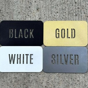 K&ouml;nnte beinhalten: Vier rechteckige Metallschilder mit abgerundeten Ecken, jedes mit einem lasergeschnittenen Wort. Das Schild oben links ist schwarz mit dem Wort BLACK, oben rechts gold mit GOLD, unten links wei&szlig; mit WHITE und unten rechts silber mit SILVER.