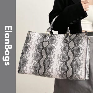Könnte beinhalten: Eine rechteckige Tragetasche mit grau-weißem Schlangenledermuster und schwarzen Schuppendetails. Die Tasche verfügt über zwei Tragegriffe, die mit goldfarbenen Beschlägen befestigt sind. Der Text ElanBags ist vertikal in Weiß auf der linken Seite gedruckt.