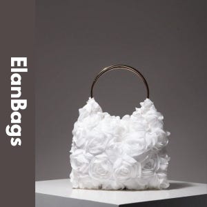 Puede incluir: Un bolso de mano blanco cubierto con aplicaciones de rosas de tela en capas que presenta un asa circular única de metal en tono dorado. El texto ElanBags está impreso verticalmente en blanco en el lado izquierdo sobre un fondo gris.