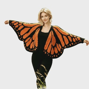 May include: A knitted cardigan featuring a vibrant orange and black monarch butterfly wing pattern. The garment has an open front design with wide, wing-shaped sleeves that extend outward, showcasing a textured stitch and bold color contrast.