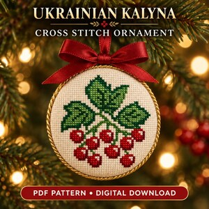 Puede incluir: Un adorno redondo de punto de cruz con un diseño de bayas rojas y hojas verdes sobre tela color crema. El adorno está bordeado por un cordón dorado trenzado y rematado con un lazo de cinta de satén rojo. El texto dice UKRAINIAN KALYNA.