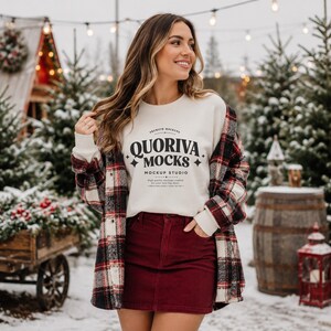 May include: A cream-colored crewneck sweatshirt featuring the black text QUORIVA MOCKS MOCKUP STUDIO with decorative star accents, worn under a red, black, and white plaid flannel button-down shirt paired with a dark red corduroy mini skirt.