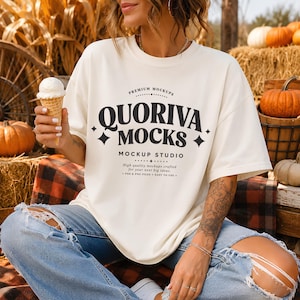 May include: An off-white short-sleeve t-shirt featuring the black text QUORIVA MOCKS MOCKUP STUDIO with decorative stars. The shirt is worn with blue distressed jeans. The graphic includes the text PREMIUM MOCKUPS and High quality mockups crafted for your next big ideas. PSD & PNG FILES EASY TO USE.