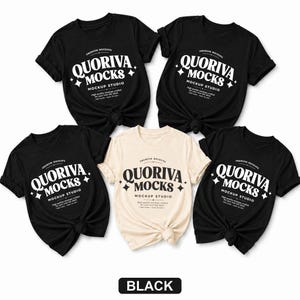 May include: Four black t-shirts and one cream t-shirt, each featuring a white graphic print that reads QUORIVA MOCKS MOCKUP STUDIO with star accents. Each shirt is tied at the bottom hem, displaying short sleeves and a crew neckline design.
