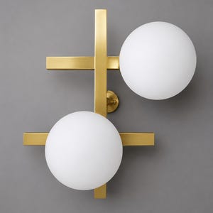 May include: A wall-mounted light fixture featuring a brushed brass metal frame with two intersecting horizontal bars and a vertical bar. Two spherical, white frosted glass globes are attached to the frame, one on the upper right and one on the lower left.