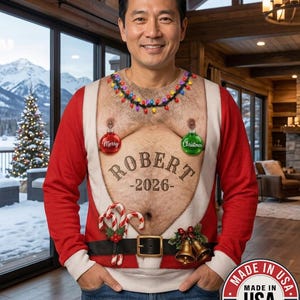 Peut inclure: Un pull à manches longues avec un motif imprimé représentant un torse nu, une guirlande de lumières de Noël colorées autour du cou, deux boules suspendues, des sucres d'orge, des clochettes et le texte "ROBERT -2026-" au centre du torse.