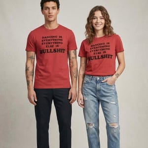 Könnte beinhalten: Zwei rote kurzärmelige T-Shirts mit dem schwarzen Text DANCING IS EVERYTHING EVERYTHING ELSE IS BULLSHIT auf der Brust. Die T-Shirts haben einen Rundhalsausschnitt und eine Standardpassform aus einfarbigem Stoff mit kräftiger Schrift.
