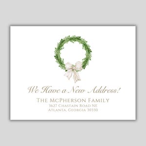 May include: A white card with a green wreath and a white bow. The text on the card reads "We Have a New Address!" followed by "THE MCPHERSON FAMILY", "3627 CHASTAIN ROAD NE", and "ATLANTA, GEORGIA 30330".