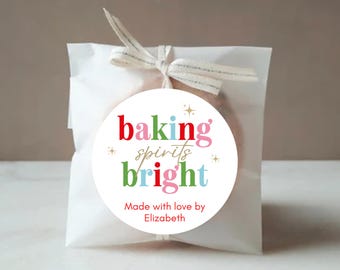 Könnte beinhalten: Eine weiße Papiertüte, die mit einem Band gebunden ist, mit einem runden Aufkleber. Der Aufkleber lautet "baking spirits bright" in Rot, Rosa, Grün und Blau, mit dem Text "Made with love by Elizabeth".